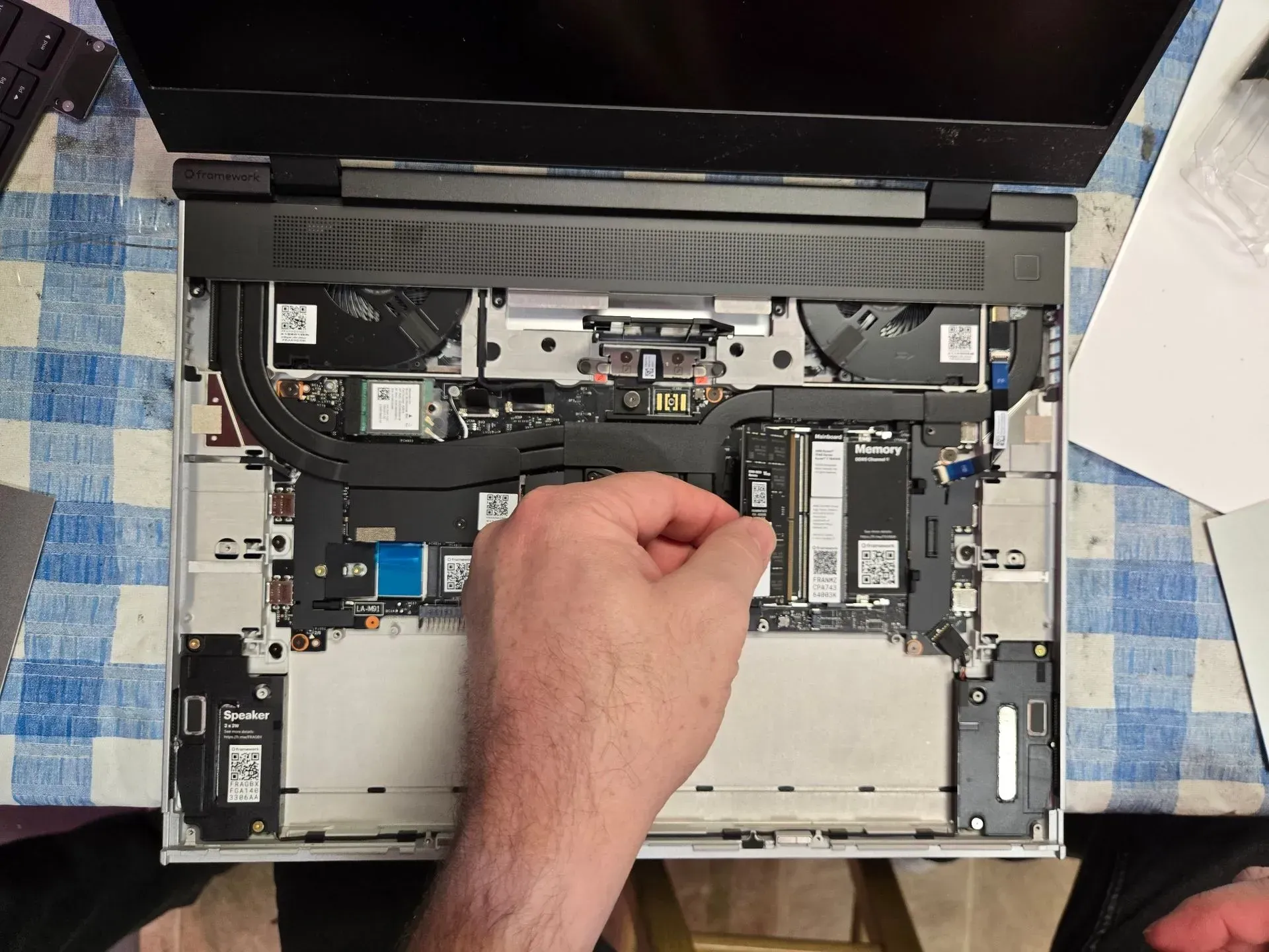 Hand holding a memory stick over the open interior of a laptop on a checkered tablecloth.