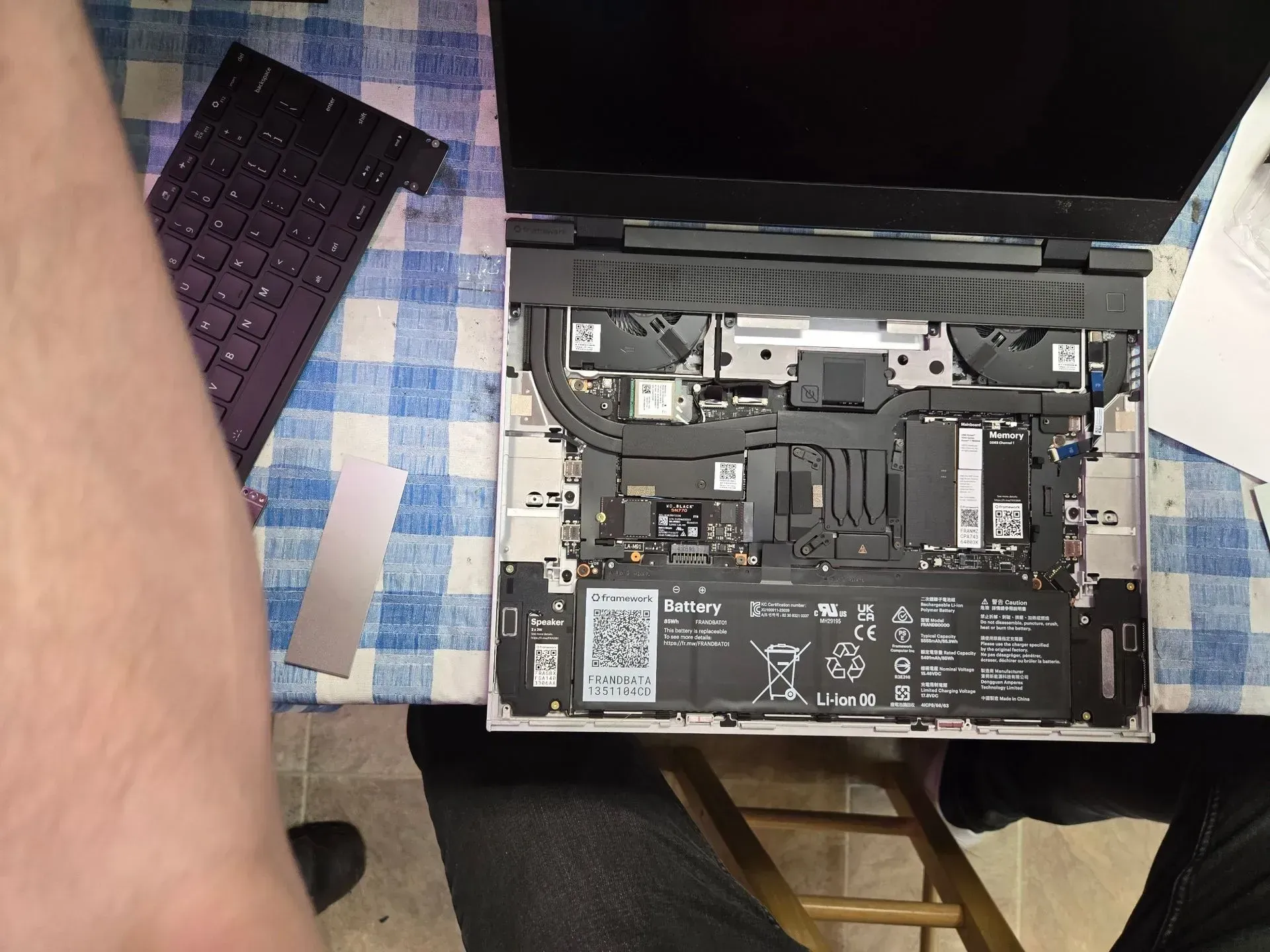 Laptop being disassembled on a blue checkered surface, keyboard detached. Internal components visible.