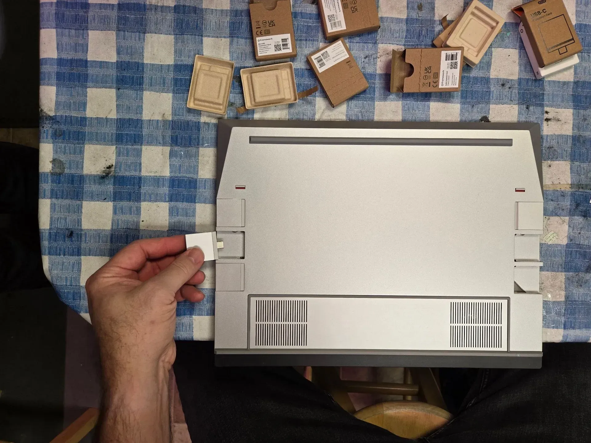 Person inserts white tab into silver electronic device, small boxes in background.