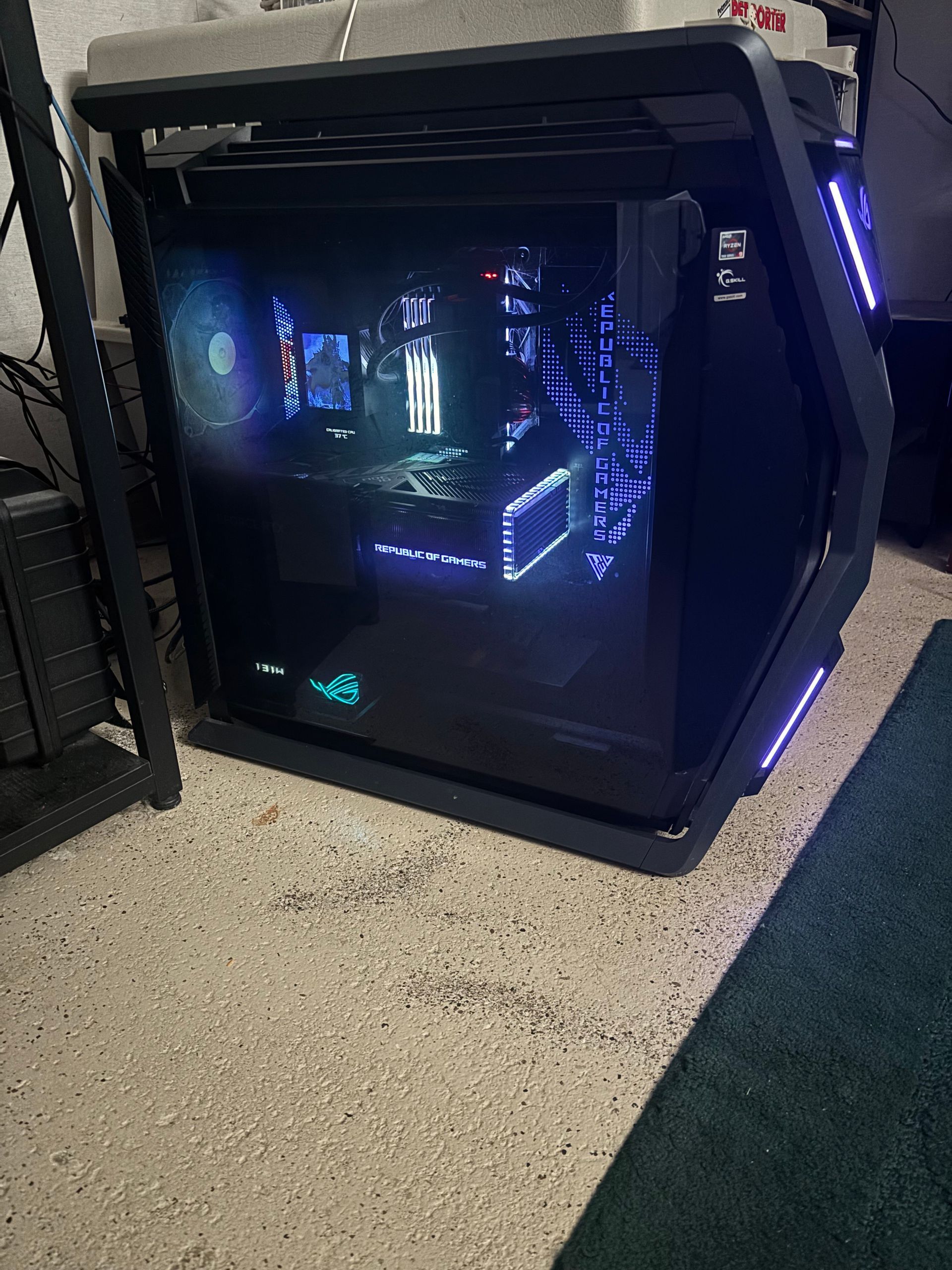 A large, illuminated black computer case with blue internal lights, sitting on a concrete floor.