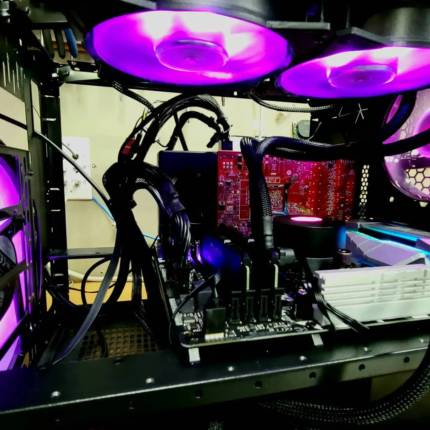 Inside of a computer, lit by purple LED fans, with black cables and a red motherboard.
