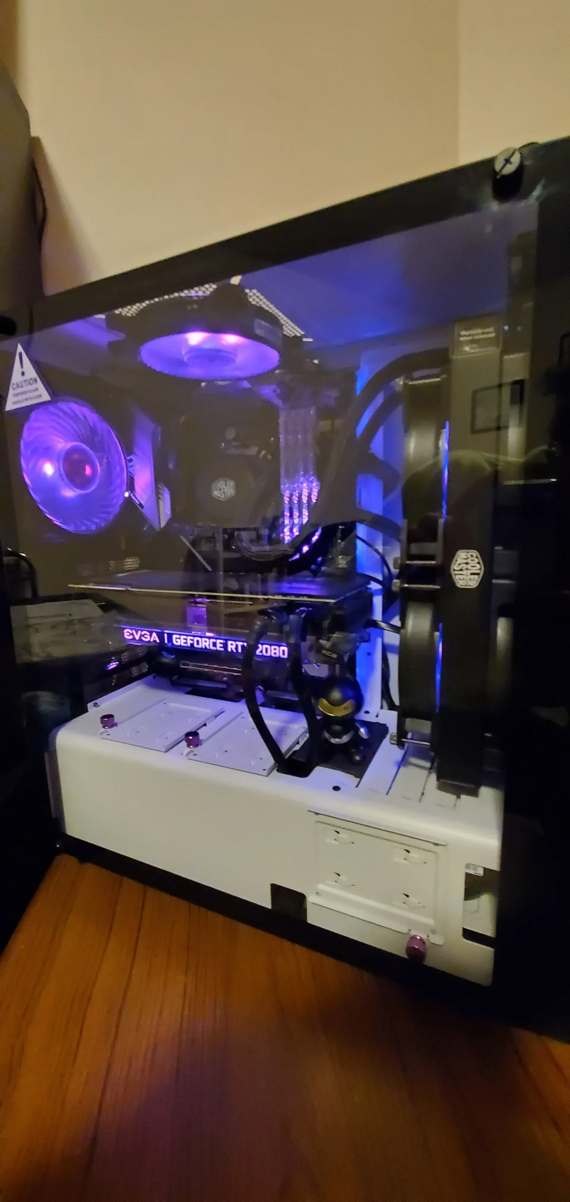 A computer tower with a transparent side panel, lit by purple and blue lights. The case is on a wooden floor.
