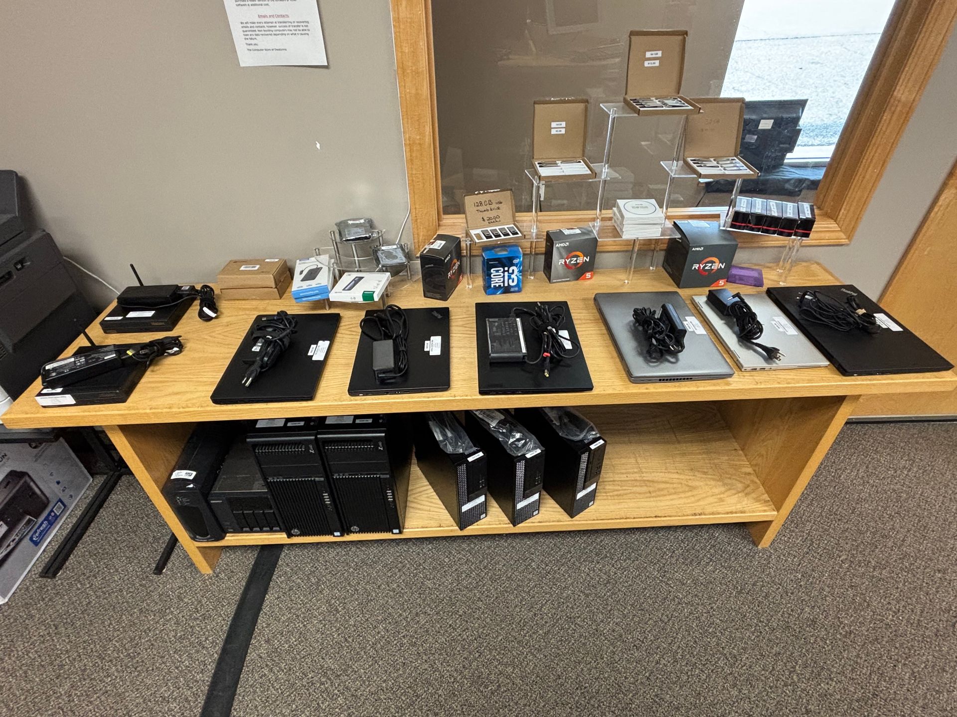 Wooden display table with electronics, including computers, phones, and accessories.