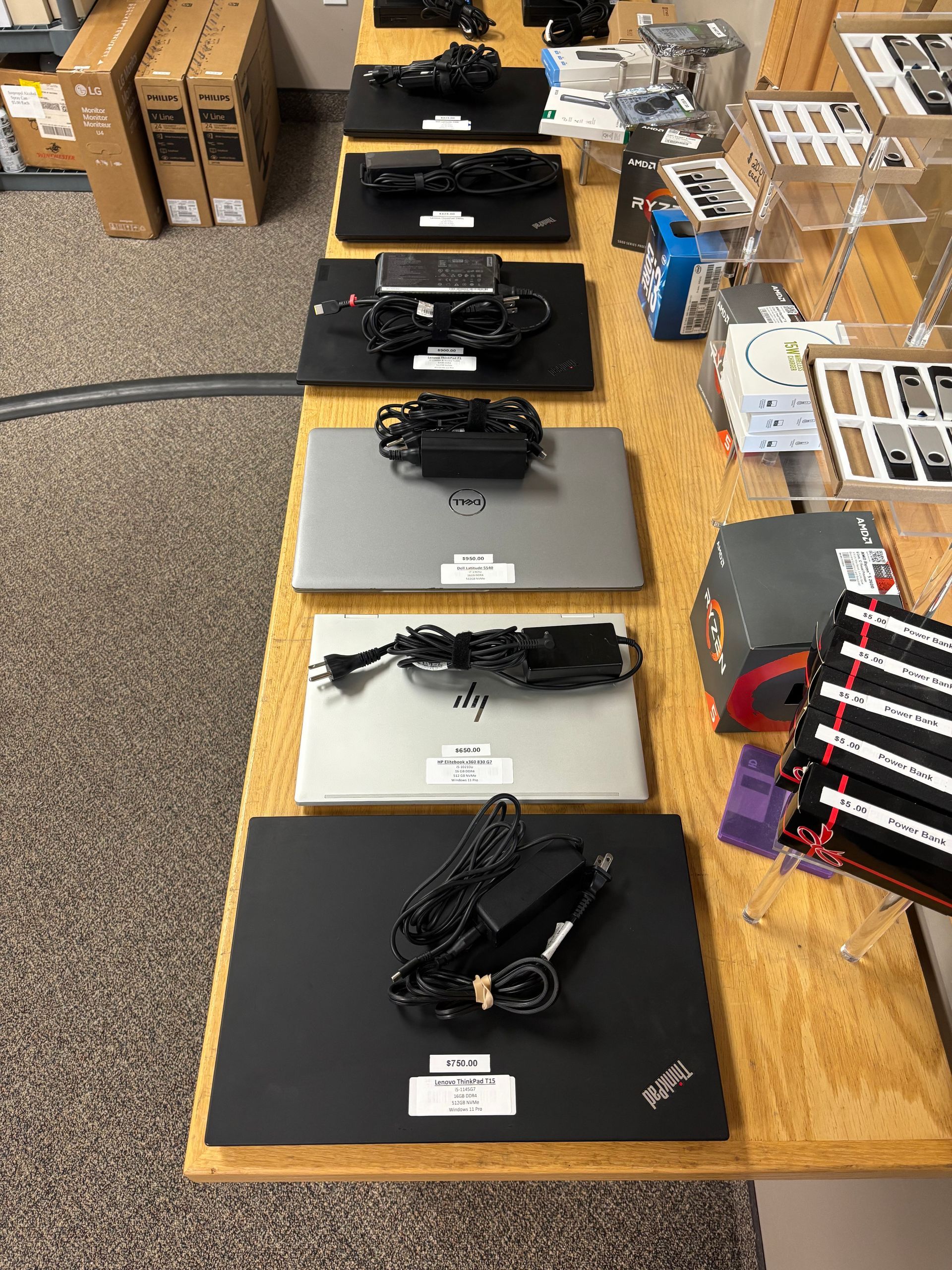 Laptops, chargers, and other electronics displayed on a wooden table in a store setting.