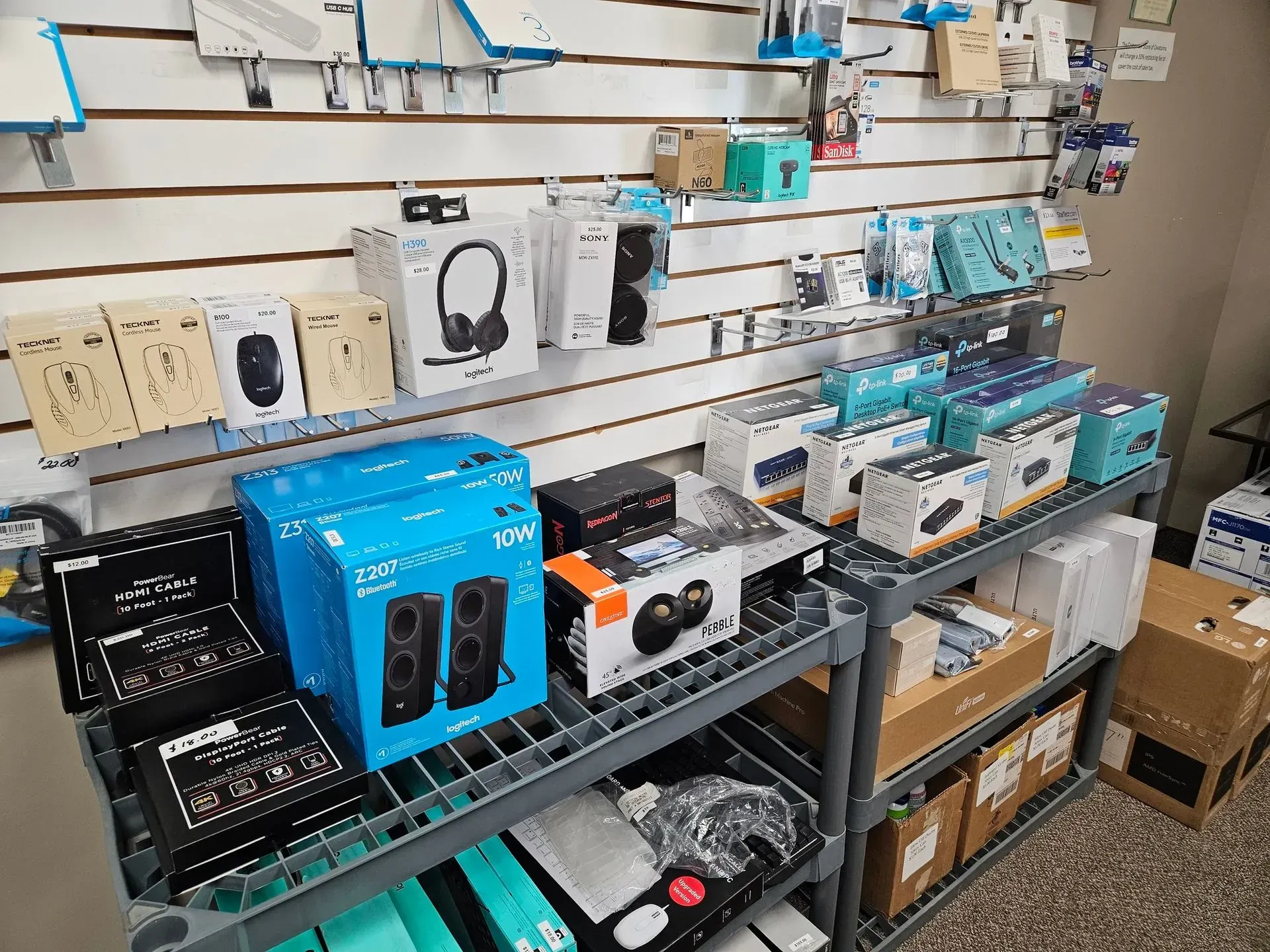 Shelves stocked with computer accessories, including speakers, headsets, and various electronics, in a retail setting.