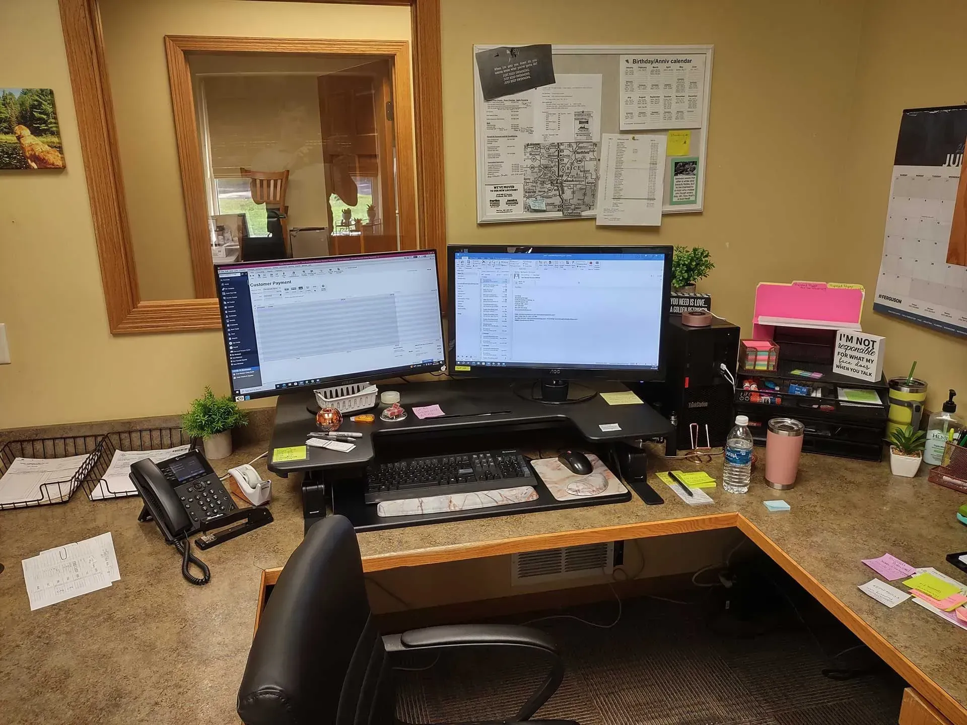 Office desk with two computer monitors, phone, keyboard, and various office supplies.