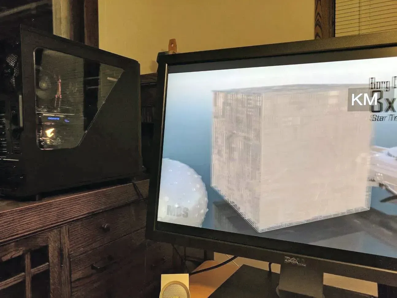 Computer tower next to monitor displaying a 3D model of a white cube. Dark wooden desk and cabinet.