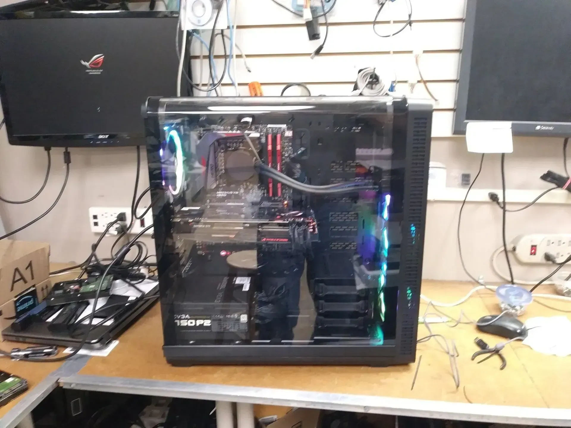 A desktop computer case with a clear side panel sits on a cluttered workbench. Inside, components glow with RGB lighting.