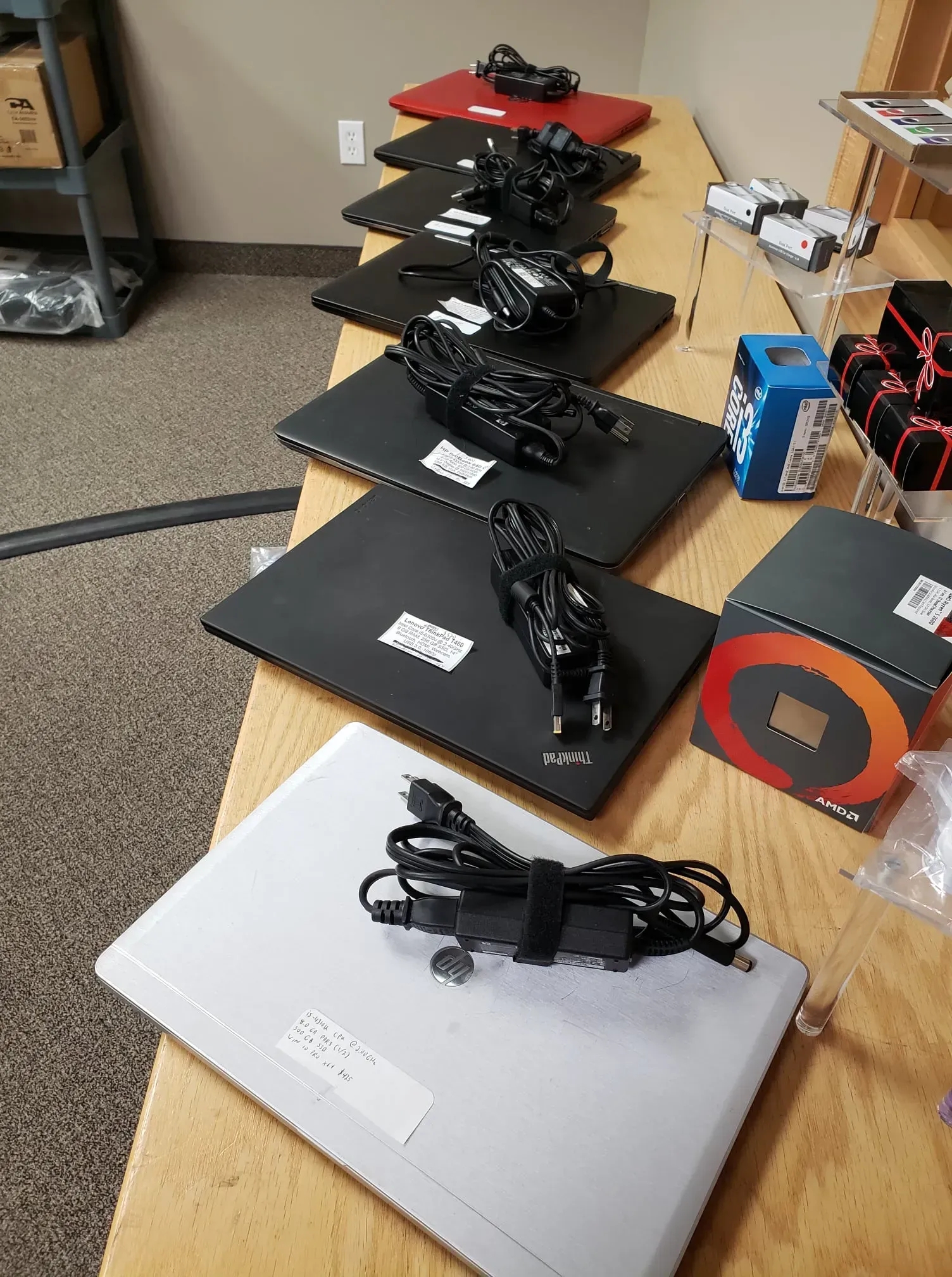 Laptops with power cords arranged on a wooden table, with an open CPU box and other electronics nearby.