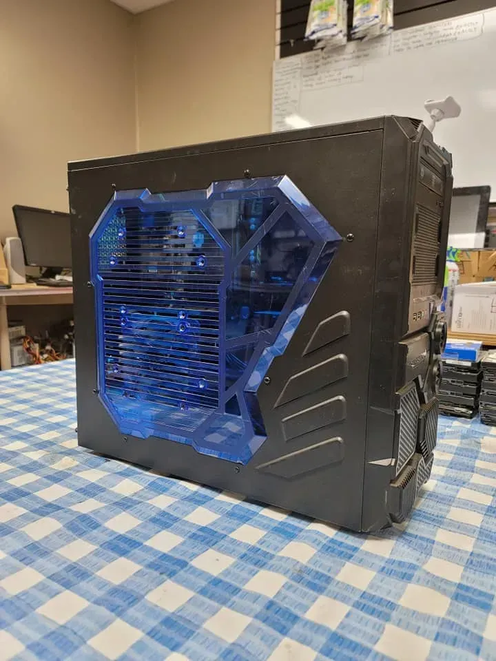 Black computer tower with a blue transparent side panel, sitting on a blue and white checkered tablecloth.