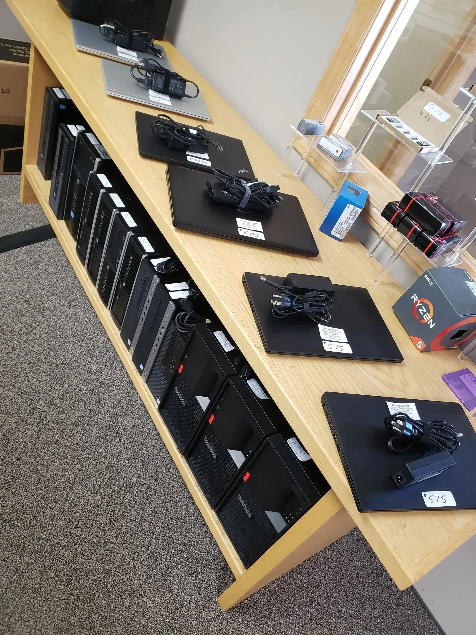 Wooden display shelf with rows of black computer towers and individual computers on mats.