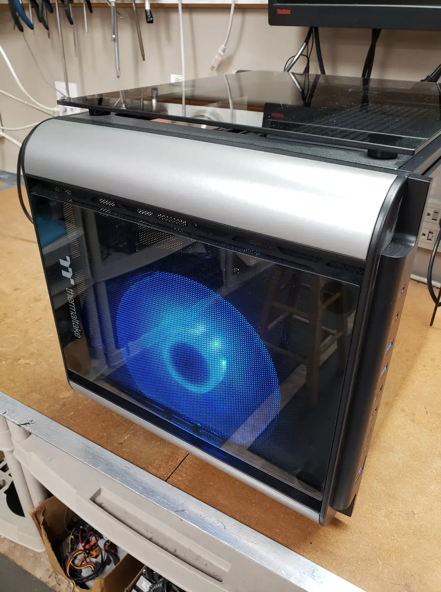 Black and silver computer case with a glass side panel, illuminating a blue, circular light pattern.