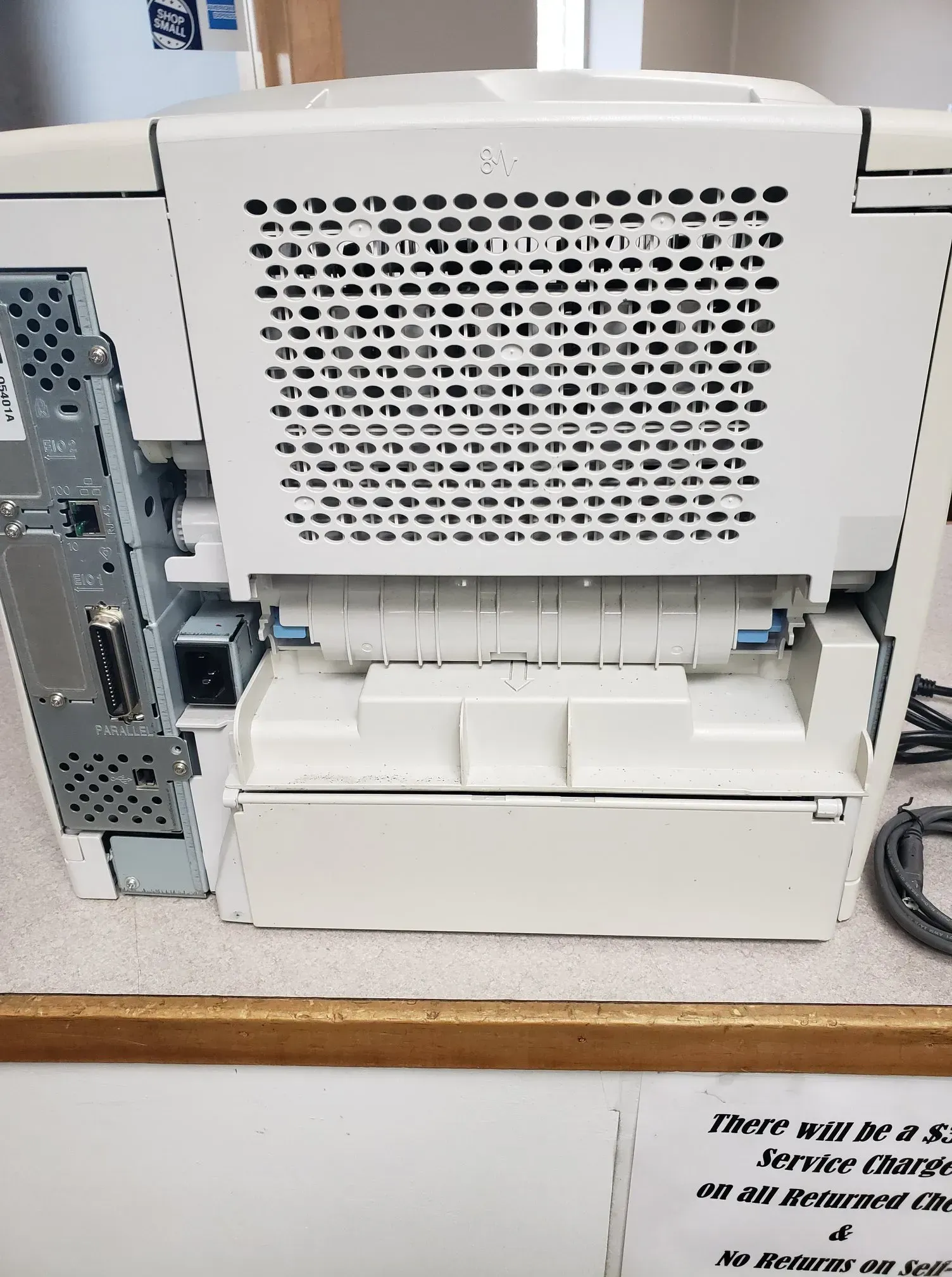 Back view of a white printer with vents, a power outlet, and a paper tray.