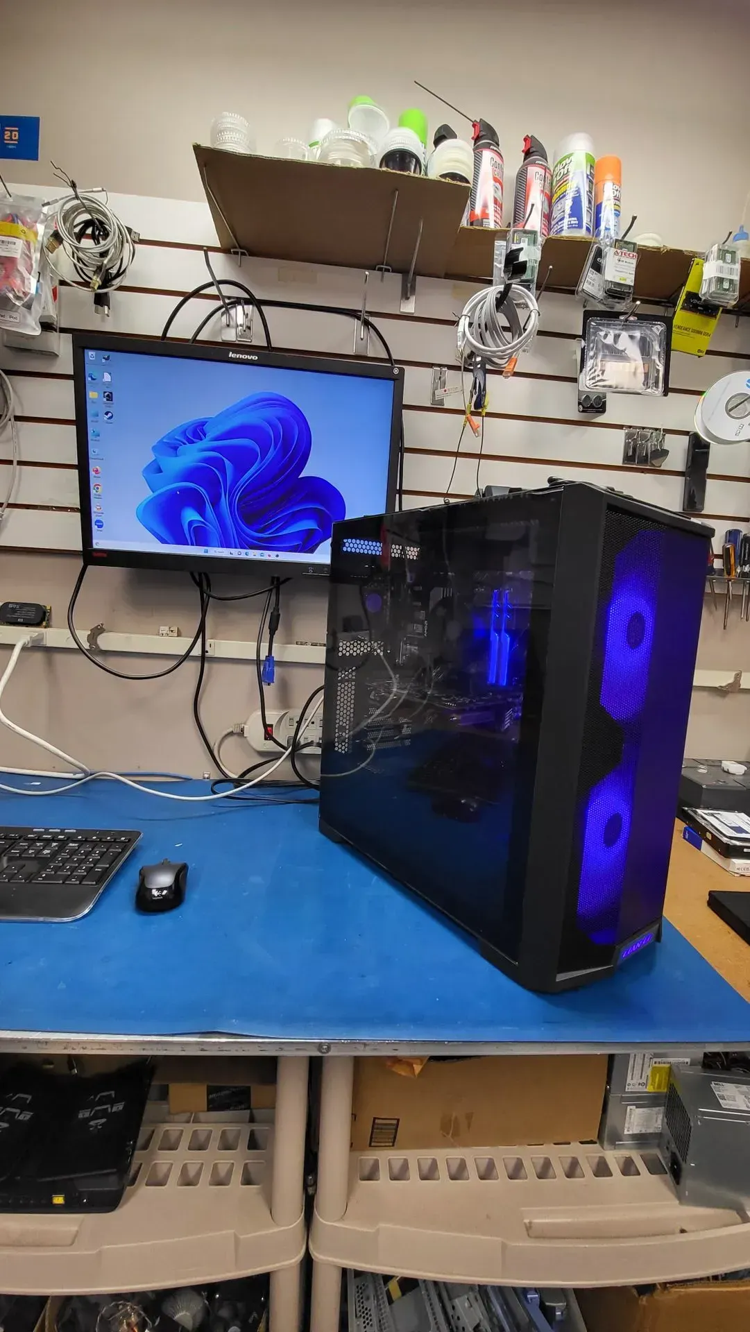 Computer setup: PC tower with blue lights, monitor displaying Windows 11, keyboard, mouse on a blue table.