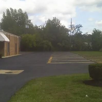 A brick building with an awning sits beside an empty parking lot featuring striped parking spaces and grassy surroundings.