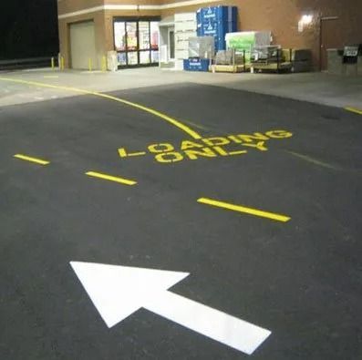 A painted white arrow on an asphalt surface leads toward a loading zone area marked with yellow text reading 