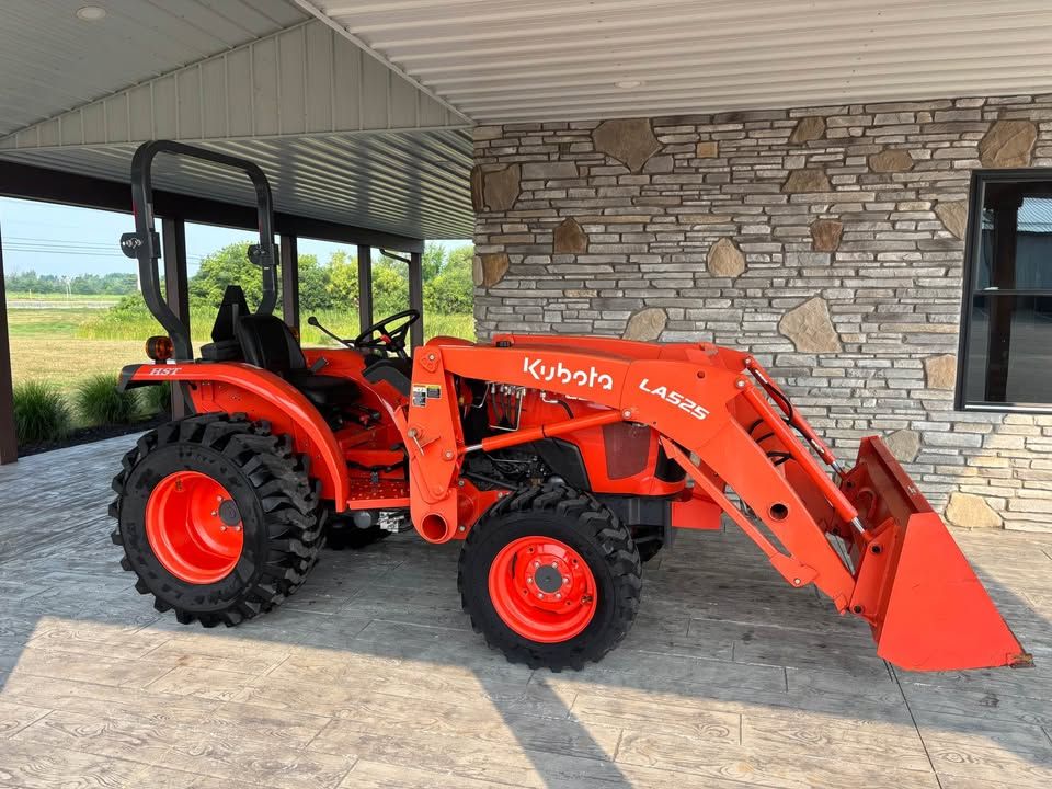 Orange Kubota tractor with front loader parked in front of a stone wall.