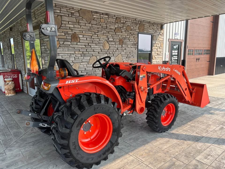 An orange Kubota tractor with a front loader parked on a paved surface in front of a brick building.