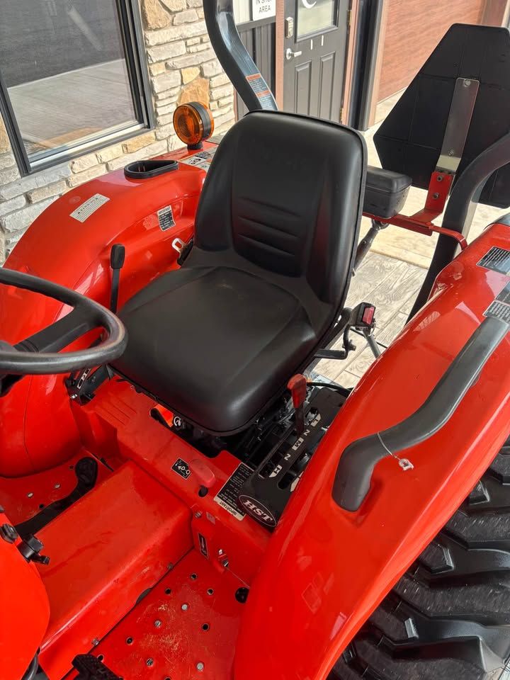 An orange tractor with a black seat and steering wheel, parked near a building.