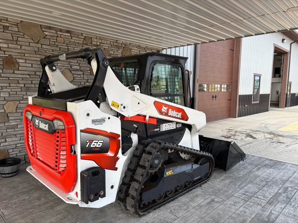 Bobcat T55 compact track loader, white and orange, parked under a covered area, showing tracks and bucket.