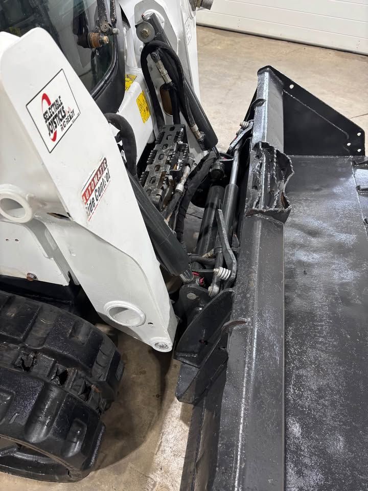 White Bobcat skid-steer loader with a black attachment, parked indoors.