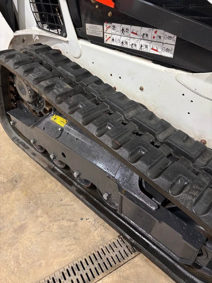 A close-up of a Bobcat skid-steer track on a concrete floor. The black track is partially visible.