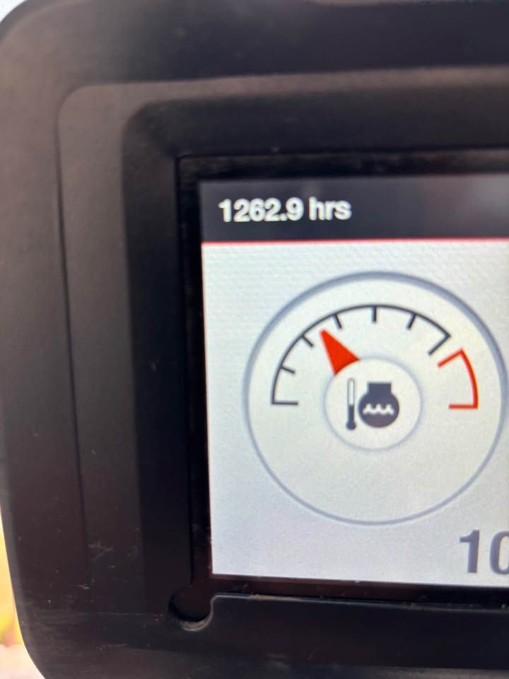 Close-up of a machine's digital display. The screen shows the operating hours (1262.9 hrs) and a temperature gauge approaching the red zone.