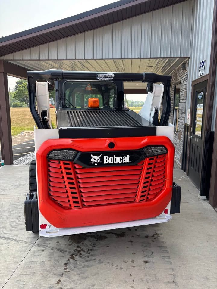 Rear view of a red and white Bobcat skid-steer loader parked in front of a building.