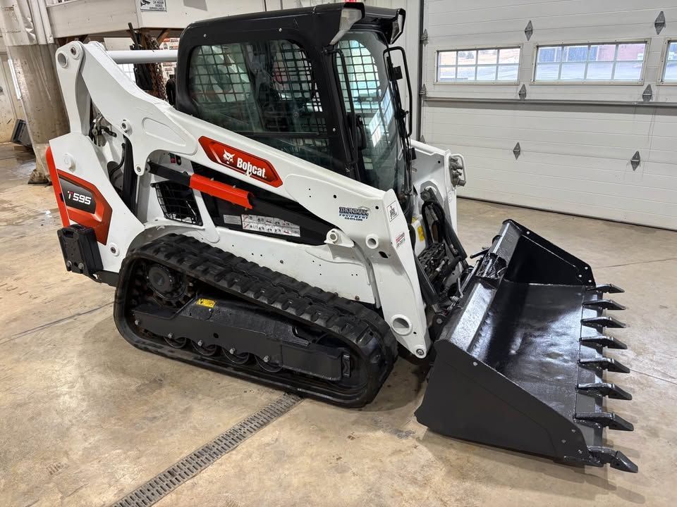 Bobcat compact track loader with a toothed bucket, indoors.