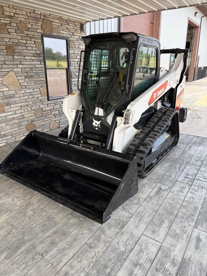 White and black Bobcat compact track loader with a black bucket parked in front of a stone-faced building.