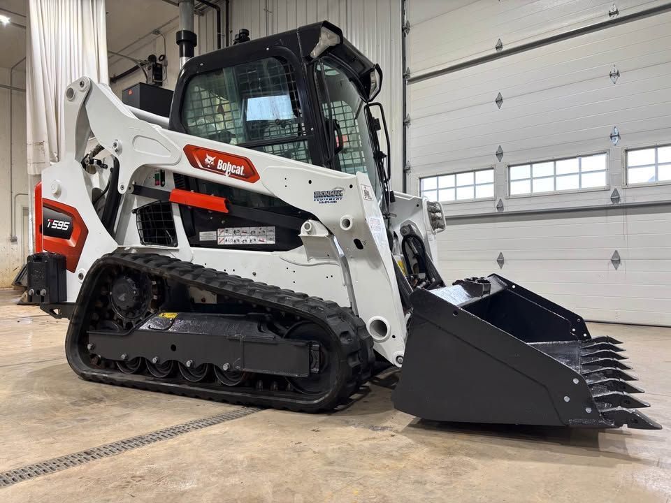 White Bobcat compact track loader with bucket in a garage.