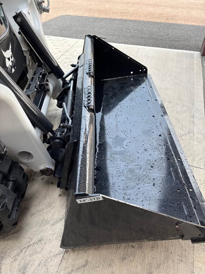 Black Bobcat skid-steer loader bucket attached to the machine, angled on concrete.