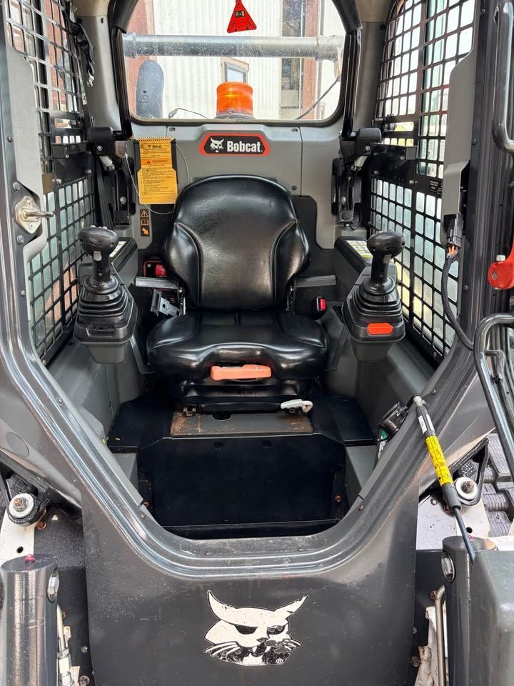 Interior of a Bobcat skid-steer loader. Black seat and controls, safety cage, and a dashboard with gauges and lights.