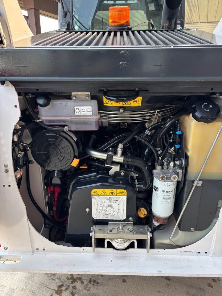 Engine of a Bobcat skid steer, showing various components like air filter, fuel filter, and fluid reservoirs.
