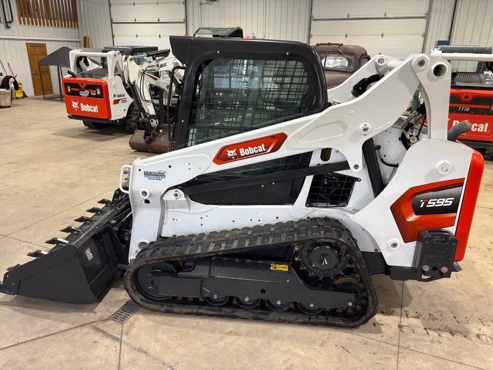White Bobcat T76 skid-steer loader with black tracks, bucket, and cab in a garage.