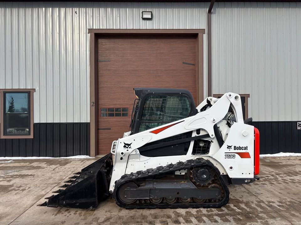 White Bobcat track loader in front of a building with a closed garage door.