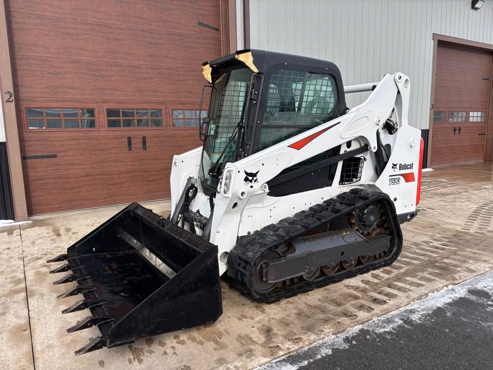White Bobcat compact track loader with bucket parked near a brown building.