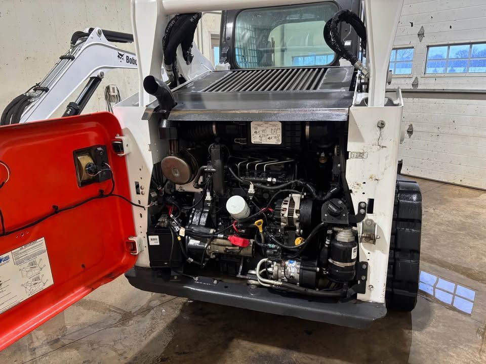Open engine compartment of a Bobcat skid steer. Red door open, revealing the engine.