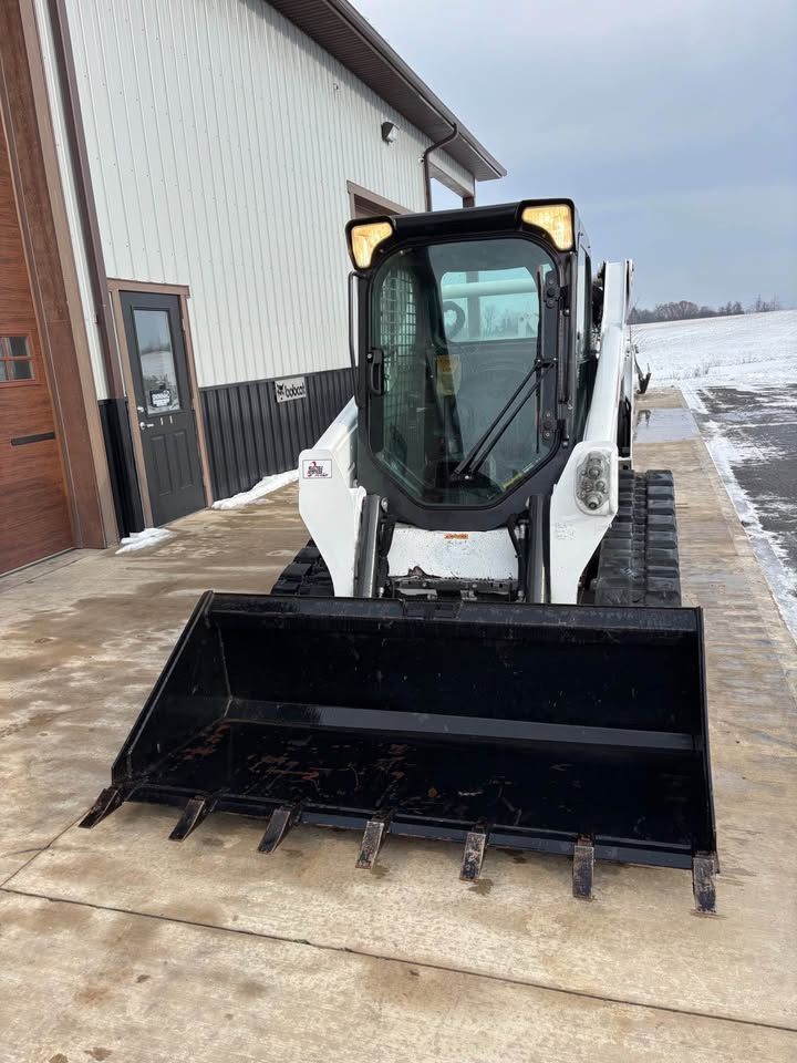 Bobcat compact track loader with black bucket in front of a white building.