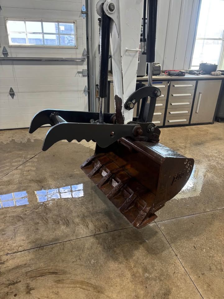 Excavator bucket with grapple claw, brown bucket, black claw, indoor setting.