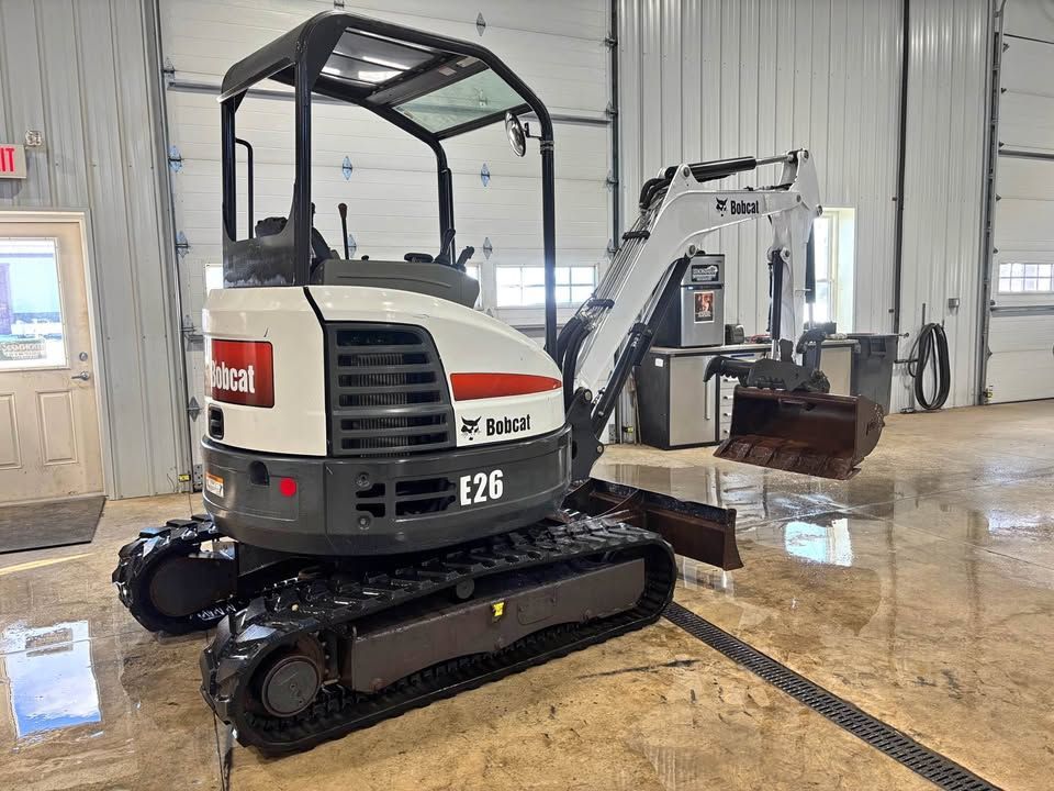 White and black Bobcat E26 mini excavator on tracks inside a building with a shiny floor.