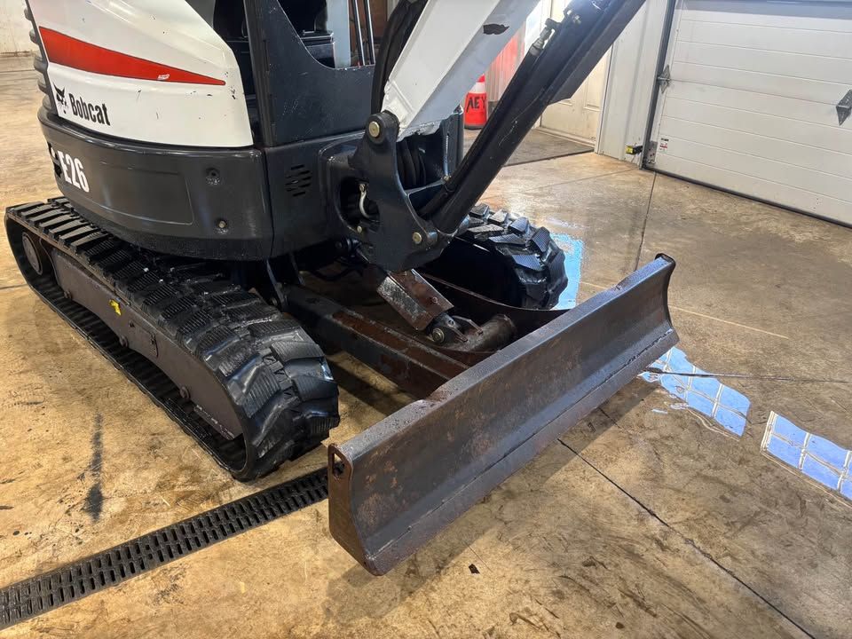 A Bobcat E26 mini excavator, angled towards the viewer, showing blade and tracks, indoors.