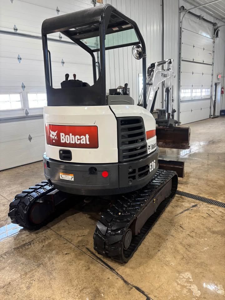 White and black Bobcat E26 mini excavator with black tracks in a garage.