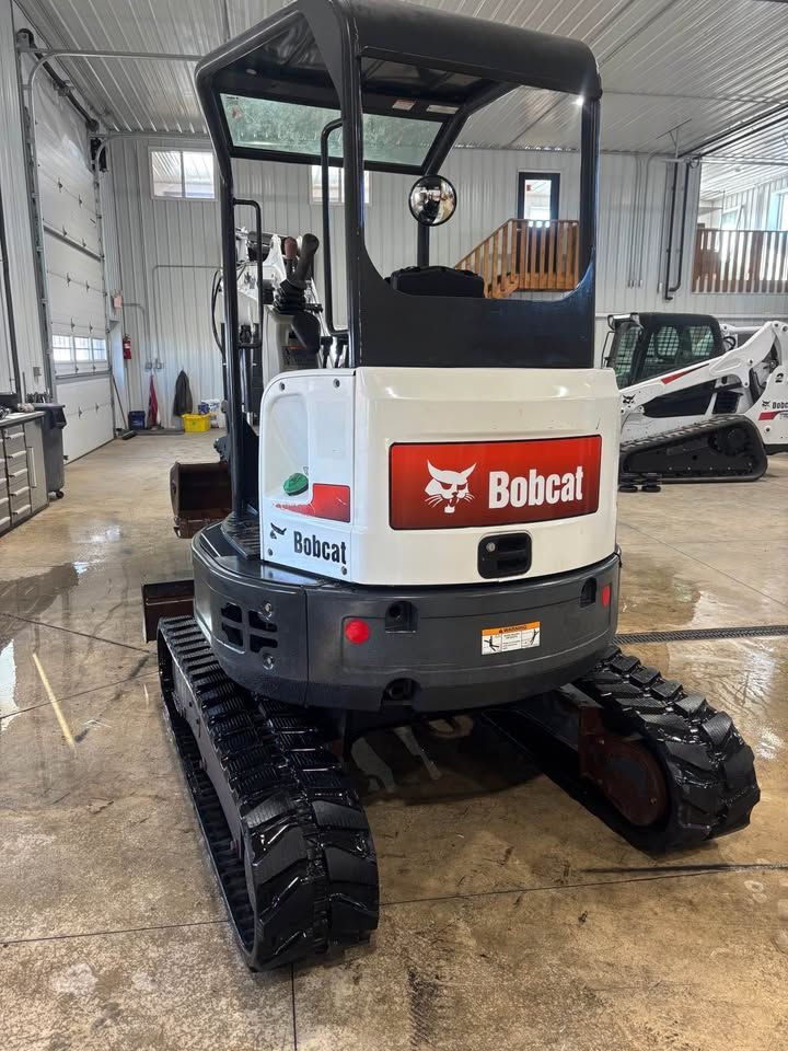 Bobcat mini excavator on a wet, light-colored concrete floor inside a building.