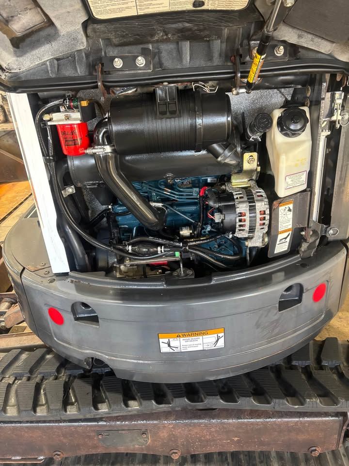Mini excavator engine compartment, black and blue engine, air filter, and fuel filter.