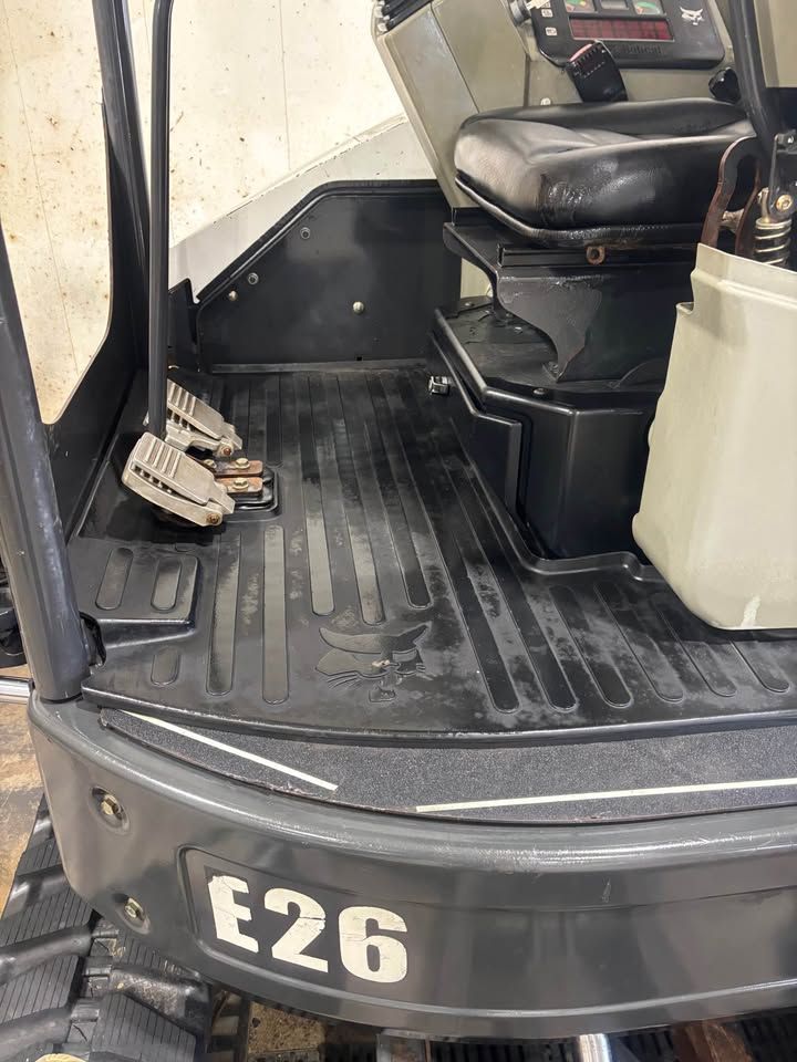 Interior of a Bobcat E26 mini excavator, featuring pedals, a seat, and the floor with the Bobcat logo.