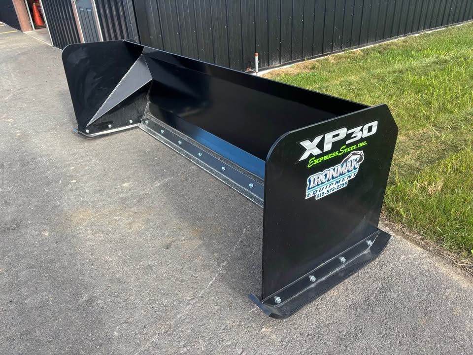 Black snow plow, model XP30, parked on pavement, green grass in background.