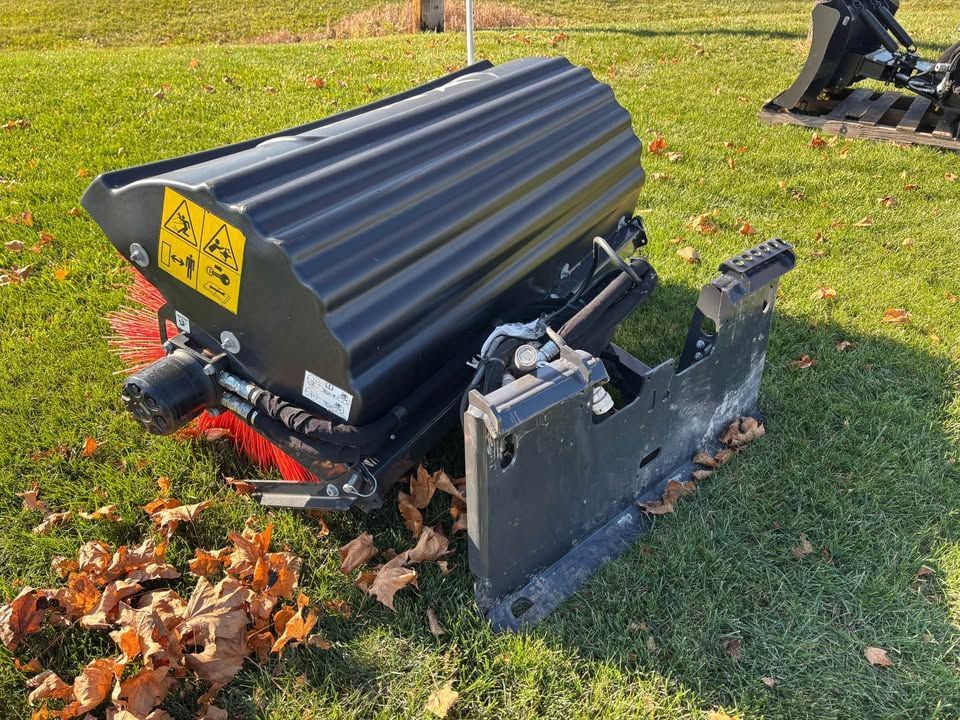 Black brush attachment on green grass, part of a tractor implement with warning labels.
