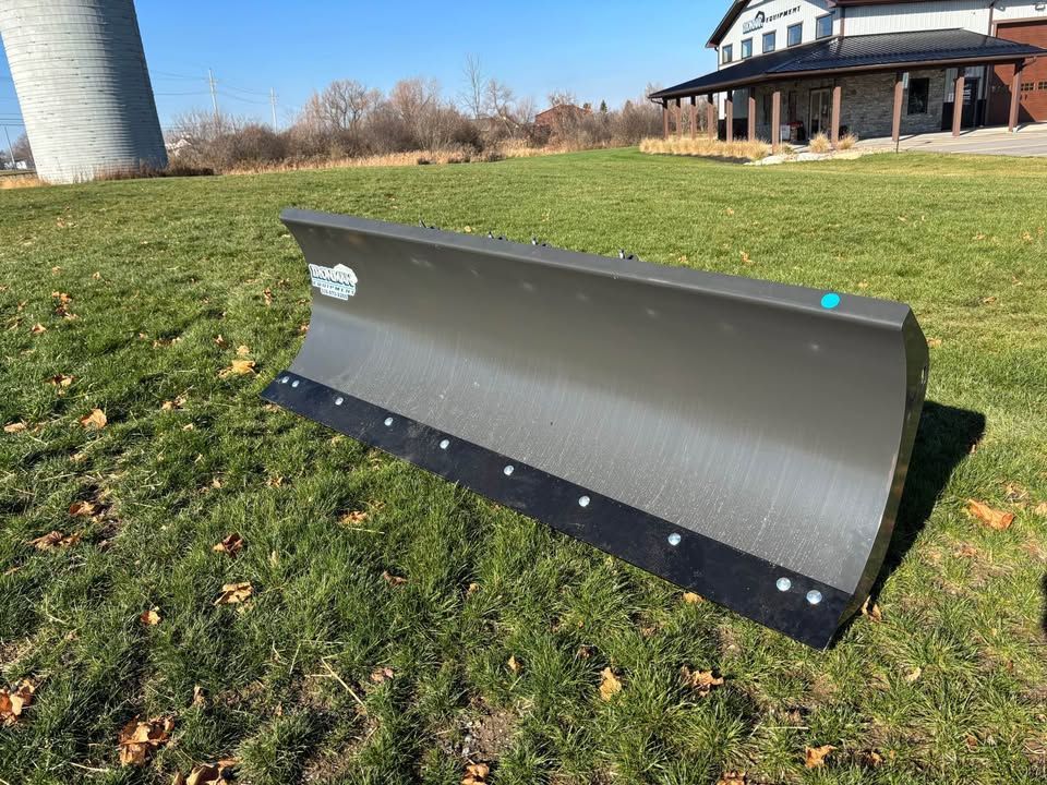 A dark gray snowplow blade on a grassy lawn with a building in the background.