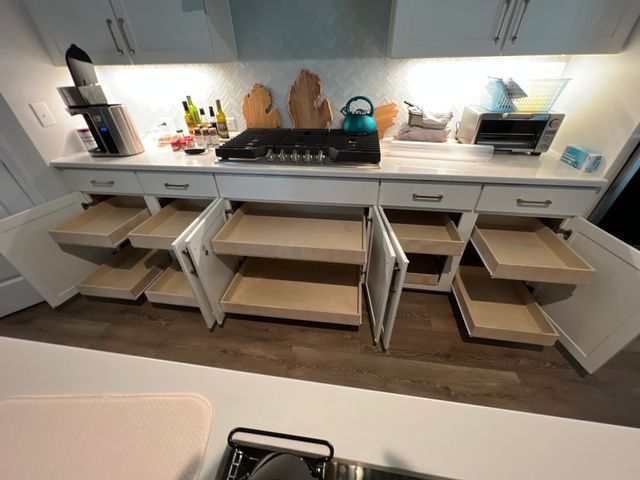 Modern kitchen with open drawers, pull-out shelves, and countertop appliances under bright cabinets